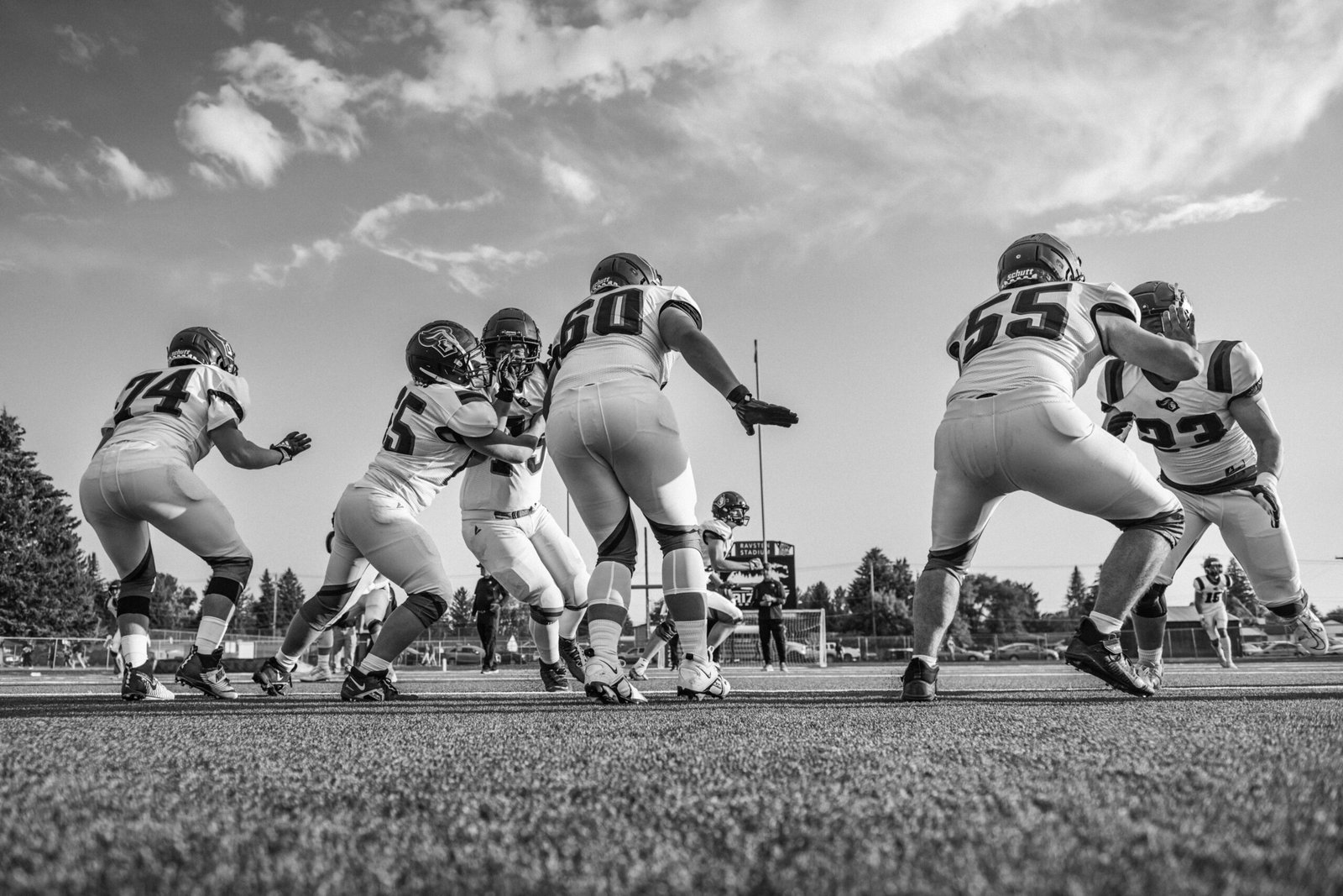 pexels-photo-34424817-34424817 Black and white photo capturing a high school football game with players in motion on the field.